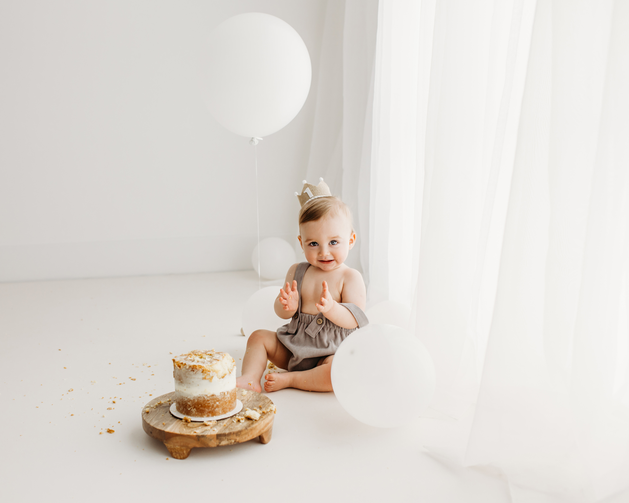 One year old baby with white balloons and cake at a cake smash photoshoot by Wirral photographer.